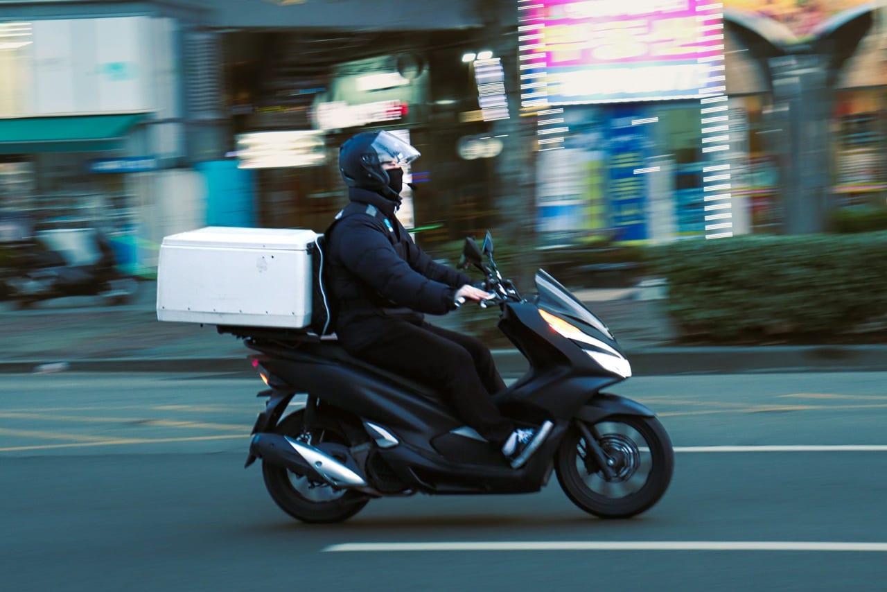 Motorizado de reparto con caja de envíos en la ciudad