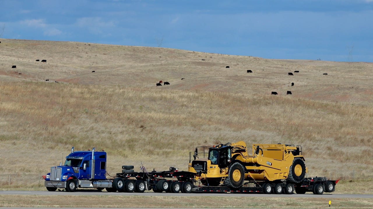 Camión con gandola lowboy trasladando una máquina amarilla por carretera